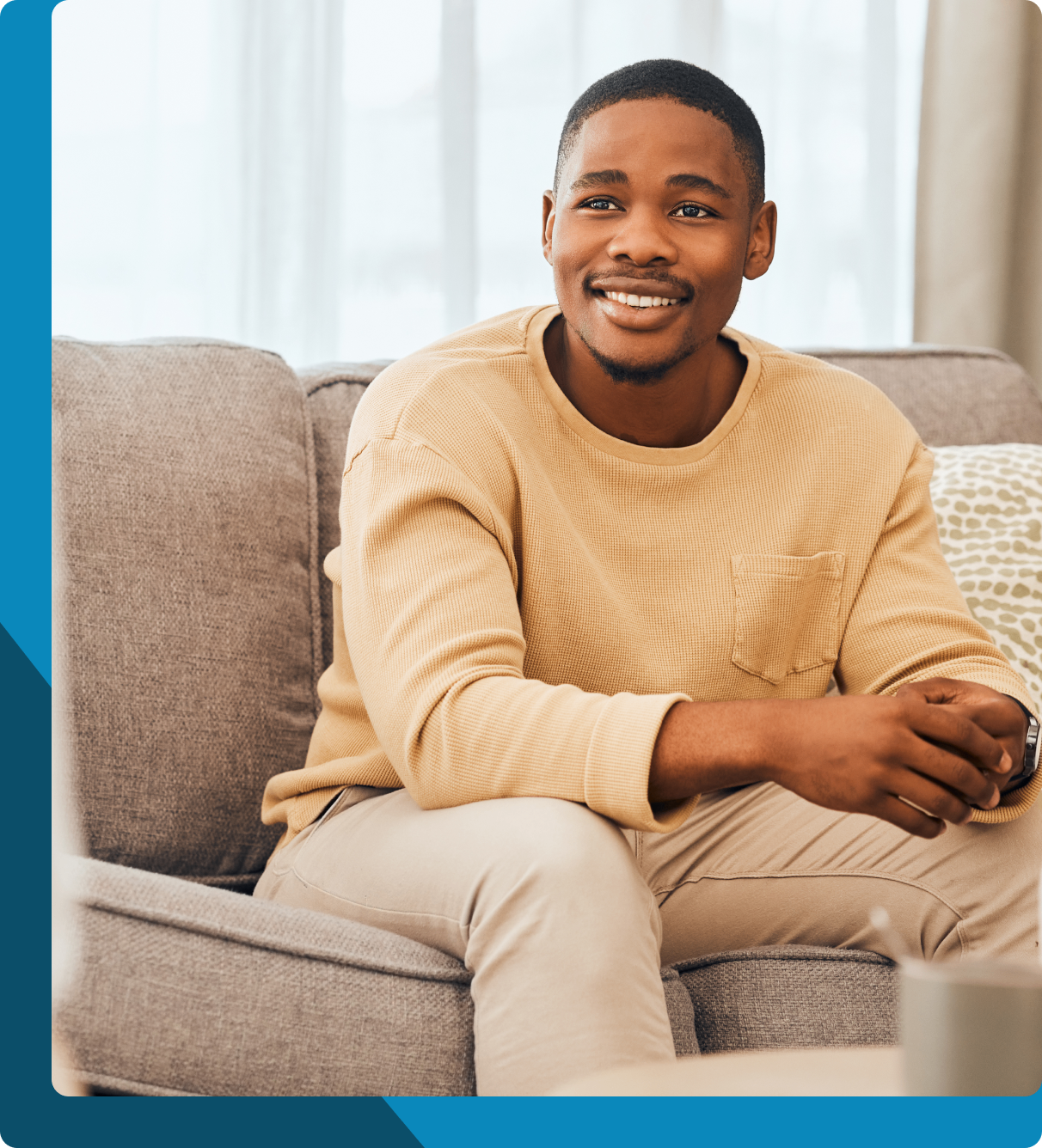 Smiling man sitting on a couch in a bright room.