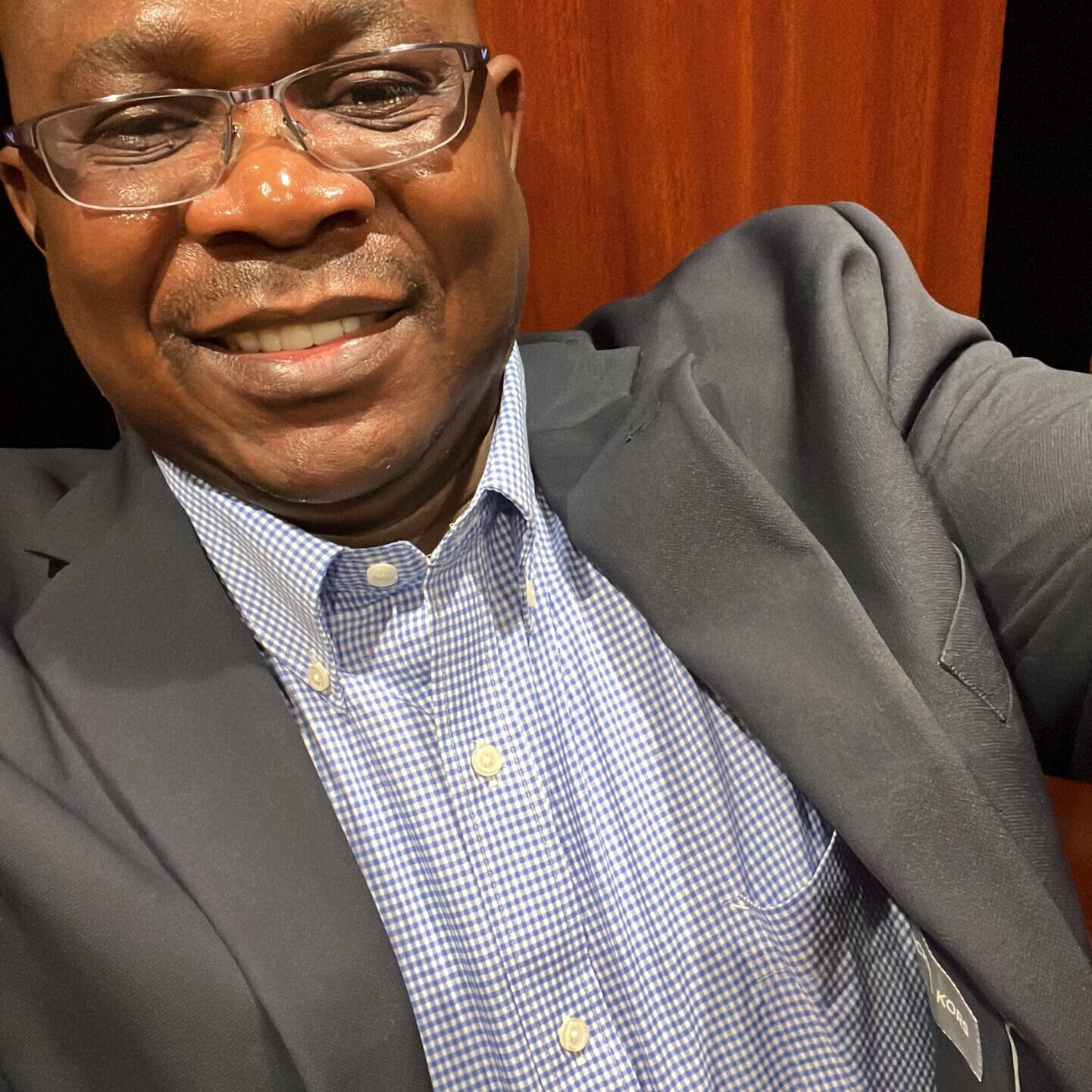 Smiling man in glasses wearing a suit and checkered shirt.